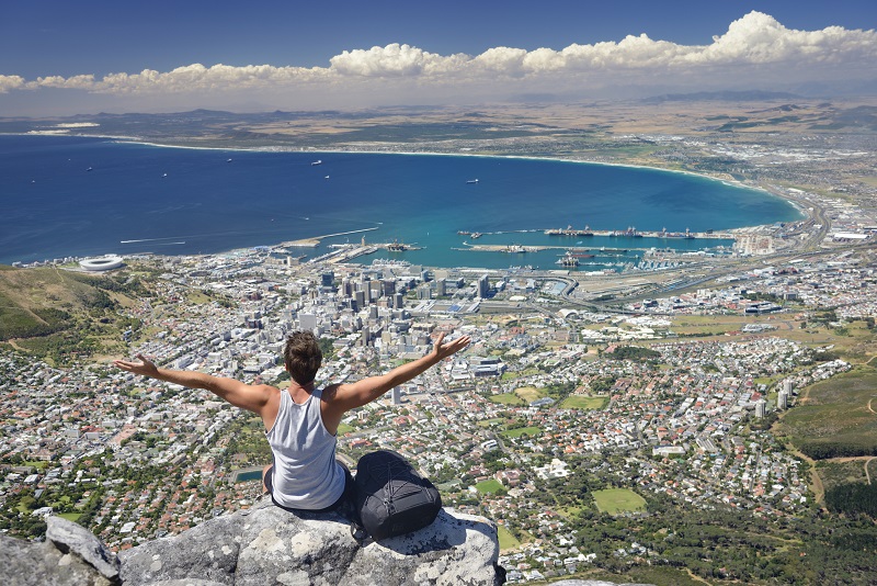 Tourist Hiker on Table Mountain overlooking Cape Town, South Africa. You can see the Cape Town Stadium on the left beside the Victoria and Alfred Waterfront. Down Town Cape Town, the Harbor all the way over Bloubergstrand to Atlantis.