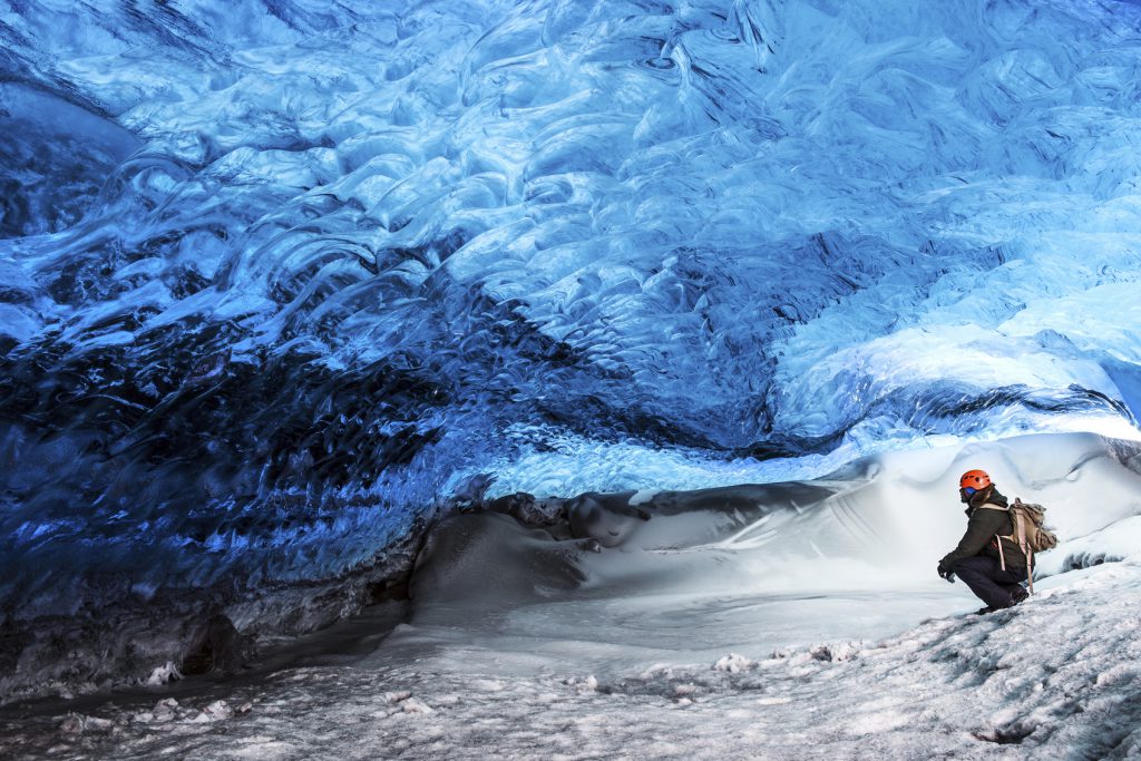 Man traveler enjoying exotic landmark, sitting in the ice cave, Skaftafell glacier, Vatnajokull National park, amazing nature of Iceland