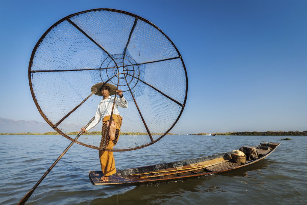 Myanmar travel attraction landmark - Traditional Burmese fisherman with fishing net at Inle lake in Myanmar famous for their distinctive one legged rowing style