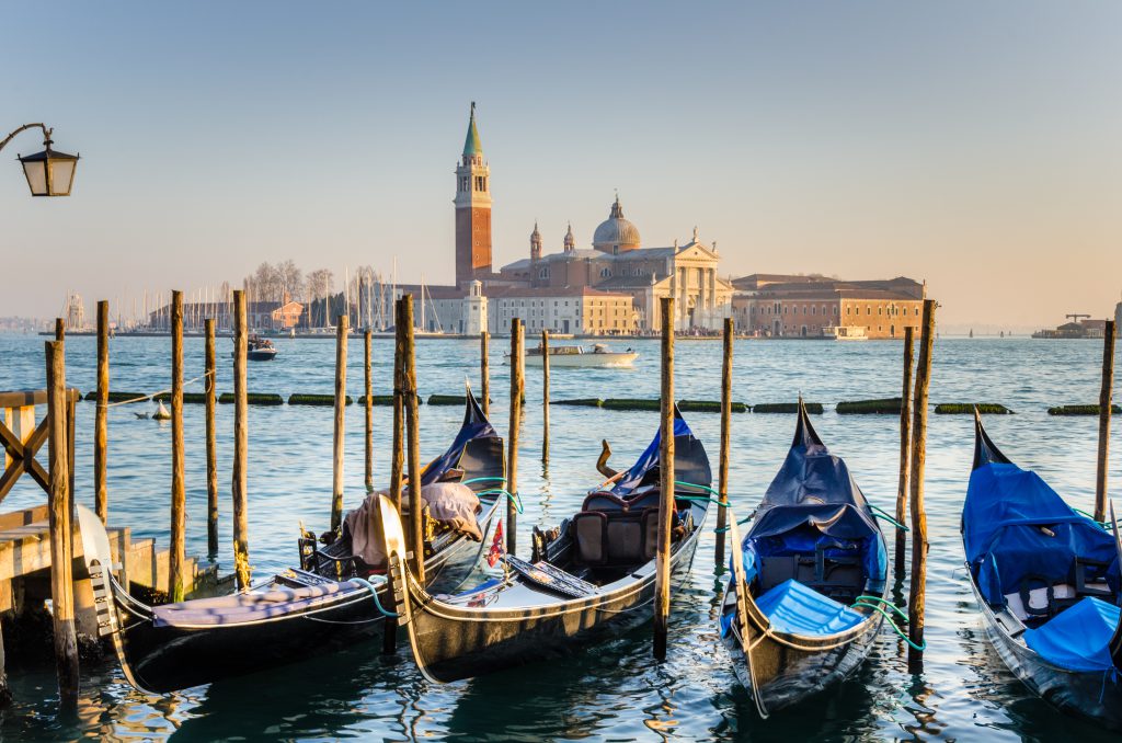 Photo of Venice at Sunset. Some traditional gondolas, tied up to the quay in Saint Mark's square, are in foreground while Saint George Island, one of the island of Venice, is visible in background.